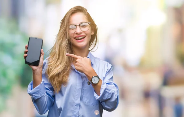 年轻美丽的金发女商人显示在孤立的背景智能手机屏幕非常高兴用手和手指指着 — 图库照片
