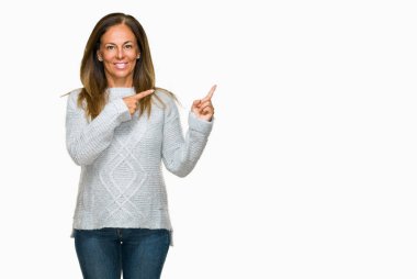 Gülümseyen ve iki elleri ve parmakları ile tarafına işaret kamera bakarak izole arka plan üzerinde kış kazak giyen güzel orta yaş yetişkin kadın.