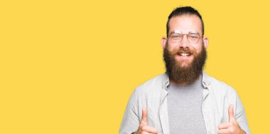 Genç Sarışın adamın gözlük başarı işareti el ile pozitif jest yapıyor giydiğini başparmak gülümseyen ve mutlu. Neşeli bir ifadeyle, kazanan jest kameraya bakıyor.