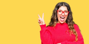 Mutlu yüz zafer işareti yaparken kameraya göz kırpıyor ile gülümseyen kırmızı gözlük takan genç güzel kadın. İki numaralı.