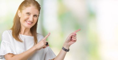 Orta yaş olgun güzel kadın gülümseyerek ve iki elleri ve parmakları ile tarafına işaret kamera bakarak izole arka plan üzerinde.