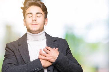 Zarif delikanlı ile gülümseyen izole arka plan üzerinde kış ceket giyen kapalı gözler ve yüzünde minnettar jest ile göğüs üzerinde eller. Sağlık kavramı.