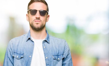 Yüzünde ciddi bir ifade ile moda güneş gözlüğü giyen yakışıklı adam. Basit ve doğal kamera bakıyor.