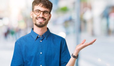 Neşeli sunulması ve kameraya bakarak avucunun ile işaret gülümseyen izole arka plan üzerinde gözlük takan genç yakışıklı adam.