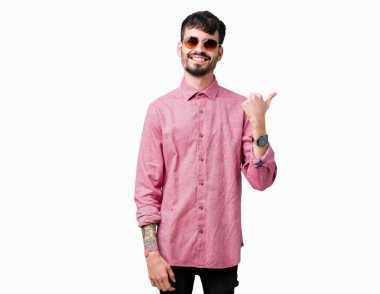 Yakışıklı delikanlı arıyor ve başparmak yanında yukarıyı mutlu yüz ile gülümseyen izole arka plan üzerinde güneş gözlüğü takıyor.