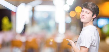 Açık el ile doğal gülümseyen girmek için davet izole arka plan üzerinde rahat beyaz t-shirt giyen genç yakışıklı adam