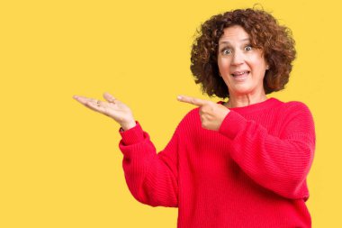 Güzel orta ager üst düzey kadın kırmızı kış kazak üzerinden hayran ve el ile sunulması ve parmak ile işaret ederken kameraya gülümseyen izole arka plan.