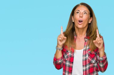 İzole arka plan üzerinde rahat forması giyen orta yaş yetişkin kadın hayrete ve yukarıya bakıyor ve parmakları ile işaret ve silah kaldırdı şaşırttı.