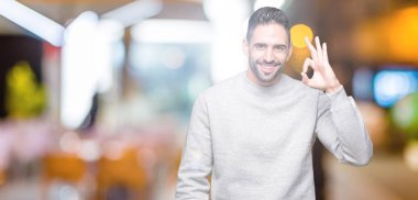 Genç yakışıklı adam izole arka plan el ve parmaklar ok işaretiyle yapıyor olumlu gülümseyen üzerinde kazak giyiyor. Başarılı ifade.