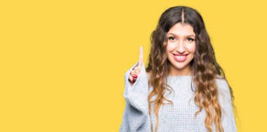 Kış kazak gösterme ve kendinden emin ve mutlu gülümseyen bir parmak ile işaret eden oktan yukarı giyen genç güzel kadın.