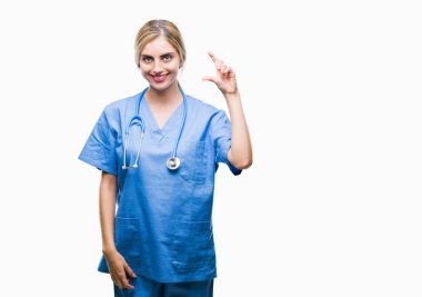 Genç güzel sarışın doktor cerrah hemşire kadın izole arka plan gülümseyen ve boyutu işaret parmaklı ararken ve kamera işi el ile kendine güvenen el hareketi yüzünden. Ölçü kavramı.