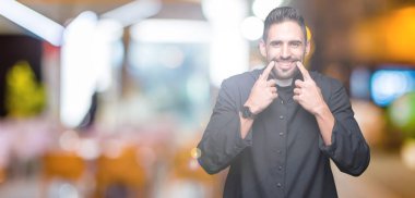 Genç Hıristiyan rahip izole üzerinde arka plan gülen açık ağız ile parmak işaret ve neşeli gülümseme zorlamadan