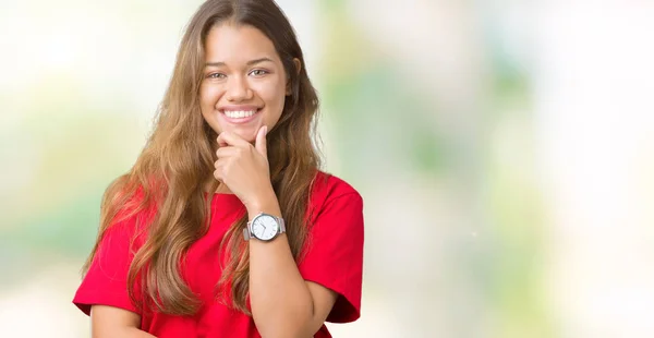 年轻美丽的黑发女人穿着红色的 T恤在孤立的背景看起来自信的镜头 微笑着交叉的手臂和手抬起下巴 积极的思考 — 图库照片