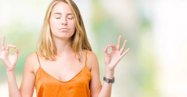 Beautiful young woman wearing orange shirt over isolated background relax and smiling with eyes closed doing meditation gesture with fingers. Yoga concept.