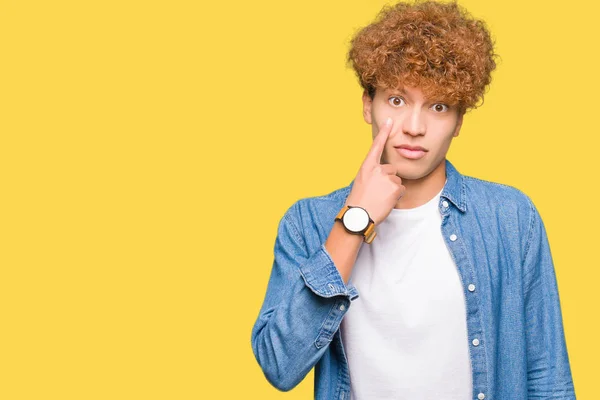 Young handsome man with afro hair wearing denim jacket Pointing to the eye watching you gesture, suspicious expression