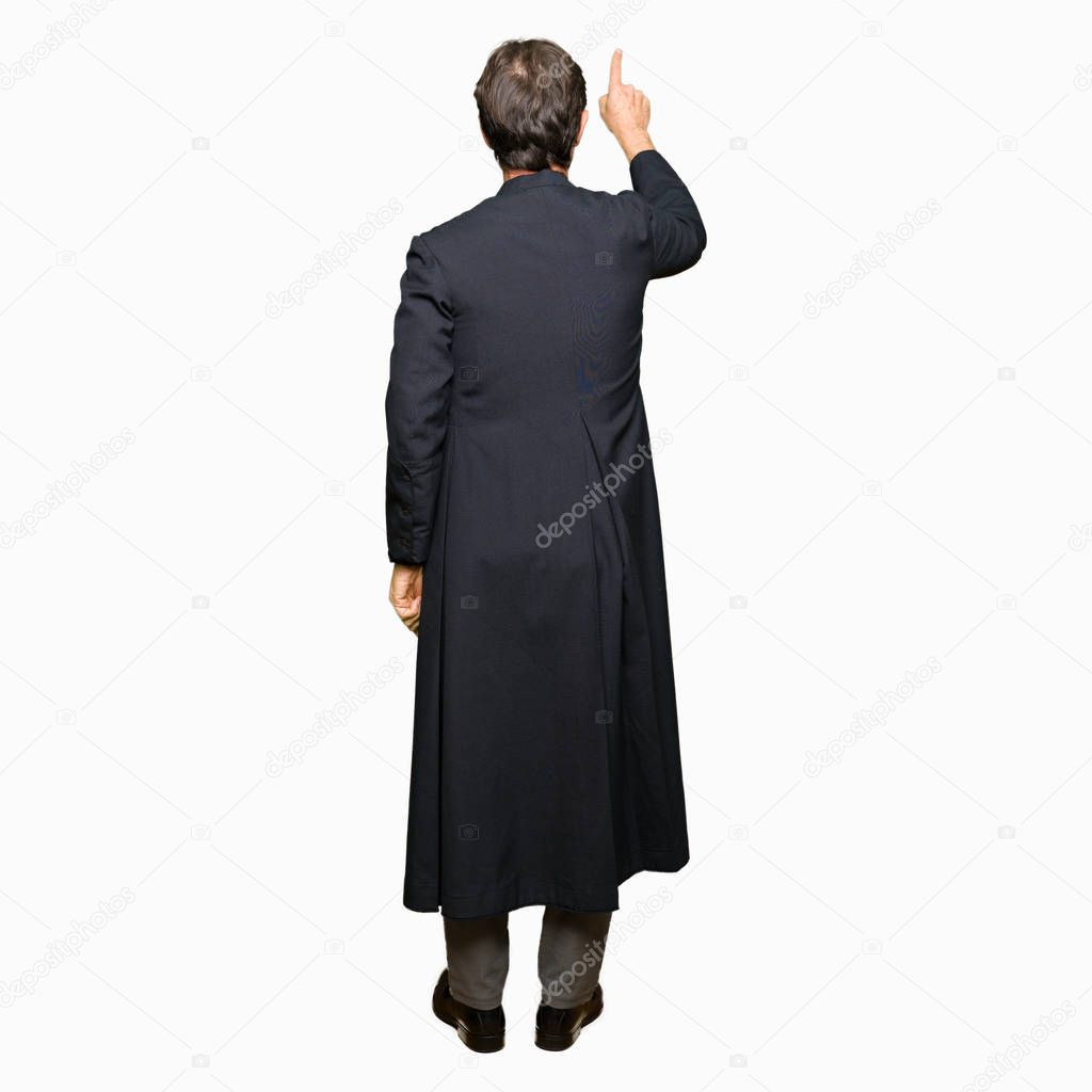 Middle age priest man wearing catholic robe Posing backwards pointing behind with finger hand