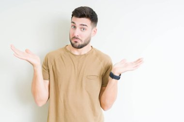 İzole arka plan clueless ve şaşkın bir ifadeyle kollar ve eller kaldırdı genç yakışıklı adam. Şüphe kavramı.