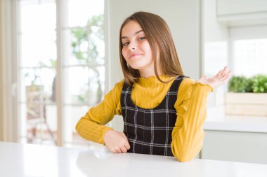 Genç, güzel, sarışın, günlük sarı süveter giyen, neşeli bir şekilde sunum yapan ve avuç içi kameraya bakan bir kız..