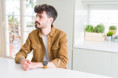 Beyaz masada oturan rahat ceket giyen genç adam yan arıyor, güvenli bir gülümseme ile doğal yüz ile profil poz rahatlayın.