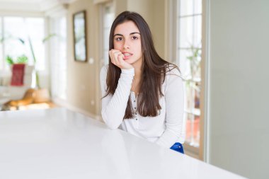 Evde beyaz masaya oturan güzel genç kadın stresli ve gergin elle çivi ısırma ağzına arıyorum. Anksiyete sorunu.