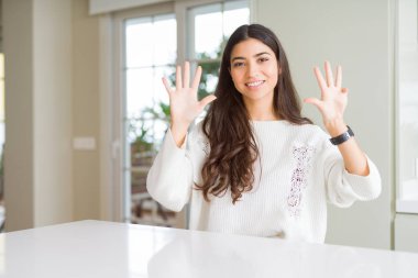 Beyaz masada evde genç güzel kadın gösteren ve parmak numarası dokuz ile işaret kadar güven ve mutlu gülümseyen.