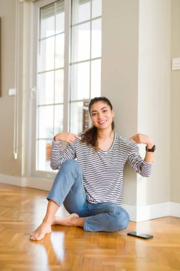 Genç güzel kadın evde katta oturan yüzünde gülümseme ile emin görünümlü, parmakları gururlu ve mutlu kendini işaret.