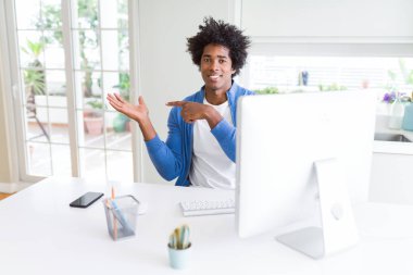 Afro-Amerikan adam bilgisayar kullanarak çalışan şaşırttı ve kameraya gülümseyerek el ile sunarken ve parmak ile işaret ederken.