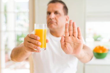 Orta yaş erkek evde ile portakal suyu bir bardak içme dur işareti ile ciddi ve kendine güvenen ifade, savunma hareketi yaparken el açmak