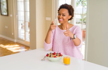 Genç Afrikalı Amerikalı kadın sabah sağlıklı bir kahvaltı yapıyor ve mutlu ve komik yüzüyle kamerayı işaret ediyor. İyi enerji ve titreşimler.
