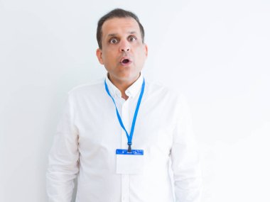Orta yaş iş adamı beyaz arka plan üzerinde kimlik kartı giyen korkuyor ve sürpriz ifade, korku ve heyecanlı yüz ile şok.