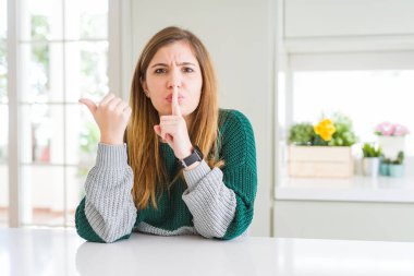 Güzel, iri yarı, sıradan çizgili süveter giyen genç bir kadın sessiz olmak istiyor. Parmakları dudaklarında ve elleri yana bakıyor. Sessizlik ve gizli konsept.