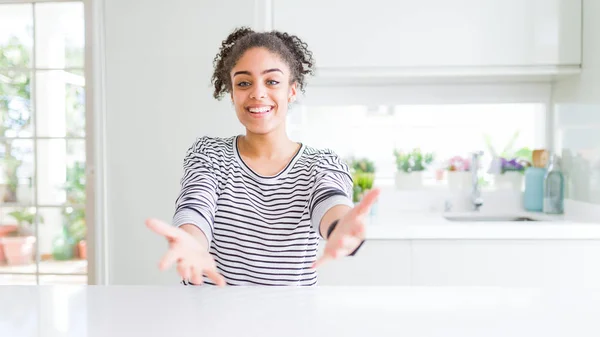 Beautiful african american woman with afro hair wearing casual striped sweater smiling cheerful offering hands giving assistance and acceptance.