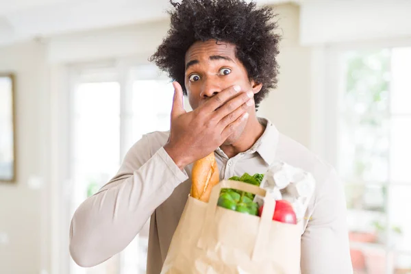 新鮮な野菜を持つ食料品袋を自宅のカバー口に持つアフリカ系アメリカ人男性は 間違い 恐怖の表現 沈黙の中で怖がって 秘密の概念にショックを受けた手で家のカバー口で — ストック写真