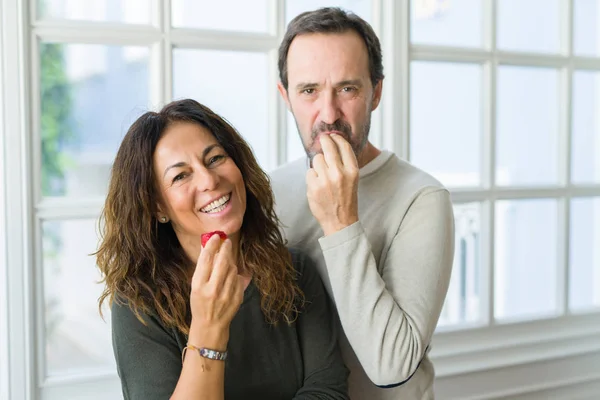 Middle age senior couple eating a fresh strawberry at home