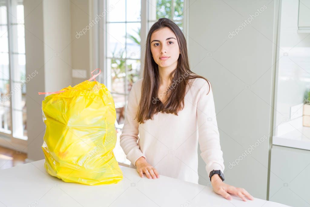 Beautiful young woman taking out the garbage from the rubbish container with serious expression on face. Simple and natural looking at the camera.