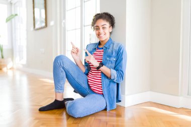 Gülümseyen ve iki elleri ve parmakları ile tarafına işaret kamera bakarak yerde oturan afro saçlı güzel genç Afro-Amerikan kadın.