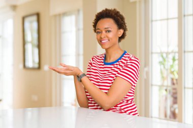 Genç ve güzel afro-amerikan kadın evinde elini ve avucunu açmış gülümseyen ve kendinden emin bir ilan veriyor.