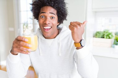 Afro-Amerikan adam tutan ve portakal suyu cam içme işaret ve mutlu yüzü gülümseyerek yan başparmak ile gösteren