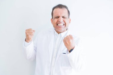Orta yaş Doktor adam beyaz arka plan üzerinde tıbbi ceket giyiyor çok mutlu ve heyecanlı silah kaldırdı, gülümseyen ve başarı için çığlık ile kazanan jest yapıyor. Kutlama konsepti.