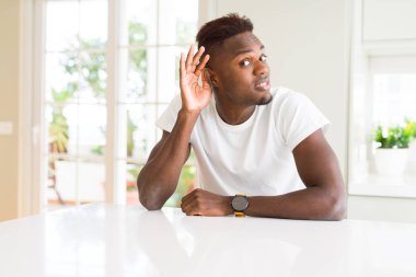 Yakışıklı afro-amerikan adam evde beyaz masada el kulağıile gülümseyerek söylenti ya da dedikodu bir işitme dinlerken. Sağırlık kavramı.