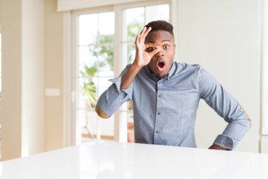 Beyaz tablo üzerinde yakışıklı Afrikalı Amerikalı adam sürpriz yüz, göz parmaklarıyla bakarak şok ok jest yapıyor. İnanılmaz ifade.