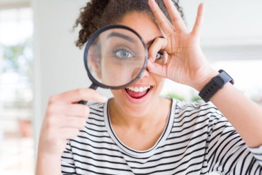 Genç Afrikalı Amerikan kadın mutlu yüz ile Büyüteç aracılığıyla görünümlü göz parmak görünümlü el ile ok işareti yapıyor gülümseyen