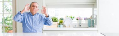 Evde yakışıklı yaşlı adam geniş açı perspektif dinlenmek ve gözleri parmakları ile meditasyon jest yapıyor kapalı gülümseyerek. Yoga konsepti.