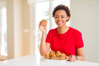 Ayakta ve diş gösterilen kendine güvenen bir gülümsemeyle gülümseyerek mutlu bir yüz ile kek genç Afro-Amerikan kadın yeme çikolata cips