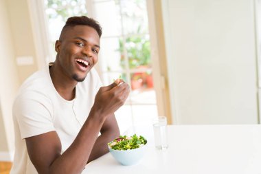 Marul, mutlu ve gülümseyerek masaya oturup yemek için çatal kullanarak sağlıklı sebze salata yemek Afrika yakışıklı genç