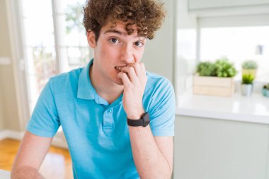 Evde rahat mavi t-shirt giyen genç yakışıklı adam stresli ve gergin elle çivi ısırma ağzına bakıyor. Anksiyete sorunu.
