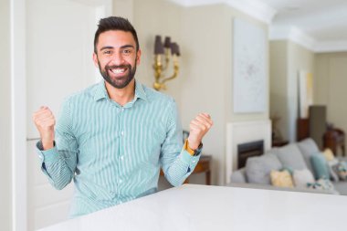Yakışıklı İspanyol adam evde sürpriz kutluyor ve kollarını kaldırdı ve açık gözleri ile başarı için şaşırttı. Kazanan kavramı.