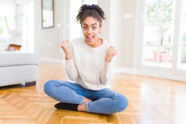 Afro saç ile güzel genç Afrikalı Amerikalı kadın yerde oturan sürpriz kutluyor ve silah ile başarı için hayran kaldırdı ve açık gözler. Kazanan kavramı.