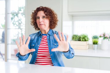 Orta yaş yaşlı kadın evde kot ceket giyen kıvırcık saçlı korku ve korku ile korkmuş ifade elleriyle jest durdurmak, şok içinde bağırarak. Panik kavramı.