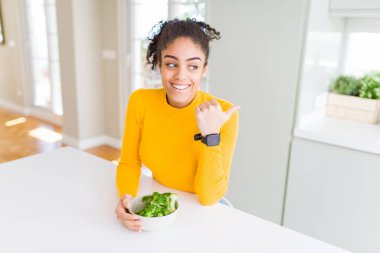 Genç Afrikalı Amerikalı kız, mutlu yüz gülümseyen yanında başparmak ile işaret ve gösteren heatlhy yeşil brokoli yeme